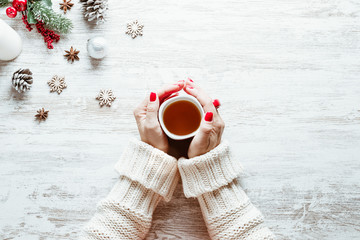 Girl hands with cup of tea on the wooden table with Christmas decorations