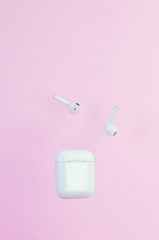 Wireless white headphones with a case on a pink background. New technologies. Trend.