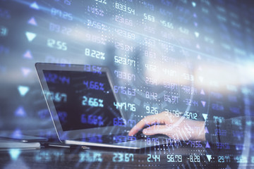 Double exposure of man's hands writing notes with laptop of stock market with forex graph...