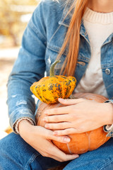 Halloween Preparaton Concept. Young woman in denim outfit sitting at garden with pumpkin harvest close-up