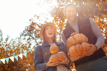 Young adult friends laughing and holding ripe pumpkin in hands