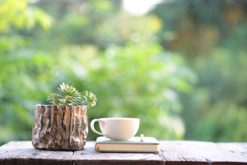 white cup with book and small cactus in wooden pot on wooden table