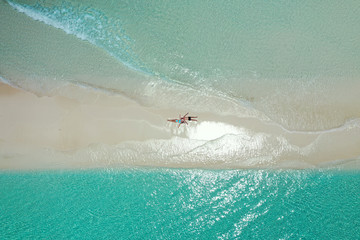 Fototapeta na wymiar romantic couple stretched on the white sand of a maldivian beach from aerial view