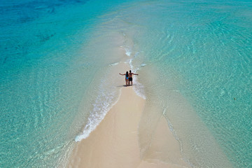 Romantic couple looking beautiful white sandy beach on sandbank surrounded by turquoise water from aerial view