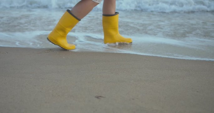 close up shot of woman legs in yellow rubber boots walking in sea with waves
