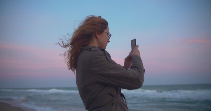 young redhead woman taking pictures with her mobile phone on the beach
