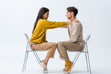 side view of attractive girl sitting on chair and touching man on white