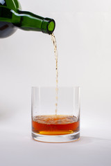 Pouring whiskey from bottle into glass with ice cubes on white background.