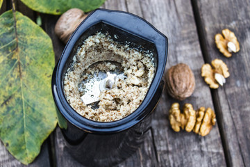 chopped walnut in a coffee grinder near the walnut kernel on an old wooden table.