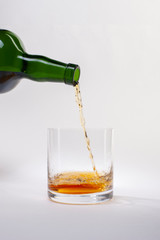 Pouring whiskey from bottle into glass with ice cubes on white background.