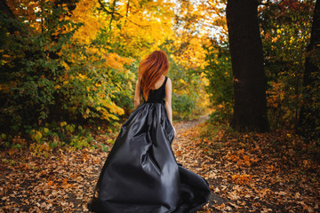 girl running in autumn orange forest. Long red hair develops in the wind.