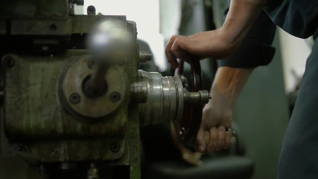 A  factory worker is operating a heavy machinery on a plant. He's spinning a big iron wheel. We ca see a lot of equipment at his work place.