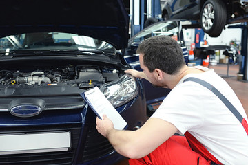 Automechaniker kontrolliert Scheinwerfer - Lichtanlage beim KFZ in der Werkstatt // Car mechanic...