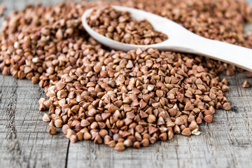 Uncooked buckwheat in a spoon on old boards. Buckwheat is used for cooking.