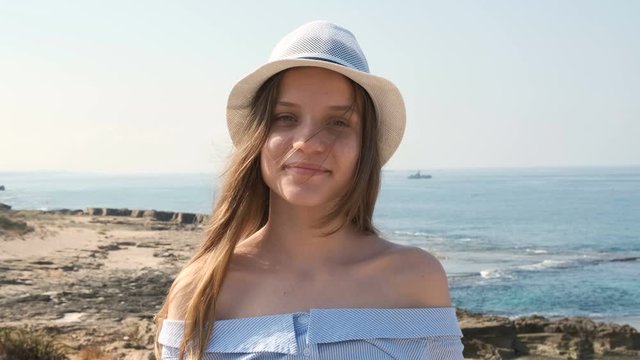 Portrait of Smiling cute teenage girl in hat. Concept israeli people, mediterranean sea coastline in background. Slow motion x2