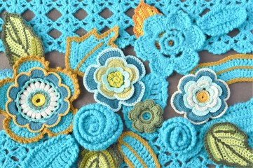Crocheted teal flowers and leaves close up on crocheted teal pattern and brown background 