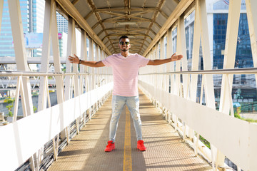 Full body shot of happy young African man with open arms on footbridge