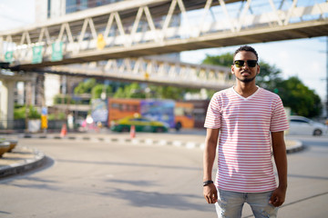 Happy young African bearded man with sunglasses in city streets