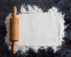 Rolling pin and white flour on a dark background