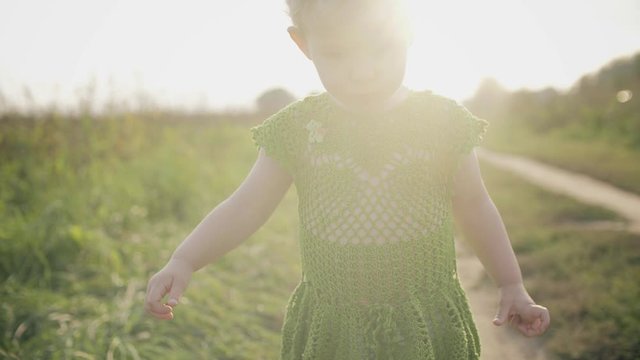 Upset baby girl walks along field pathway on a sunny day
