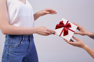 pretty woman is standing on a gray background in pc glasses and white T-shirt. Minute of happines. Someone else's hands give a gift, the girl is surprised.