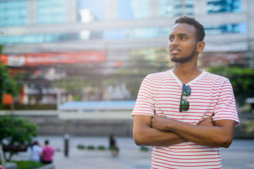 Happy young African bearded man thinking with arms crossed in the city