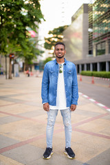 Full body shot of happy young African bearded man smiling in the city streets