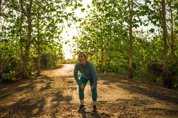 Obraz premium young happy Asian woman resting during running workout in wood on sunset . Attractive and healthy Korean girl panting after jogging in beautiful countryside road