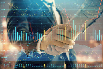 Double exposure of financial chart on cityscape background with two businessmen handshake. Concept of financial analysis and investment opportunities