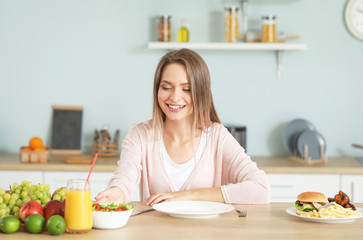 Woman with healthy and unhealthy food in kitchen. Diet concept