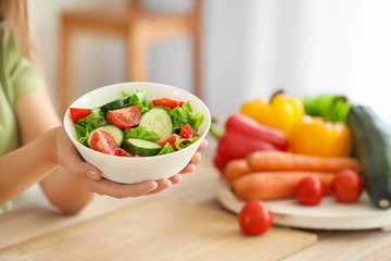 Young woman with healthy vegetable salad in kitchen, closeup. Diet concept