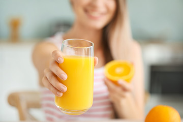 Young woman with healthy orange juice in kitchen, closeup. Diet concept