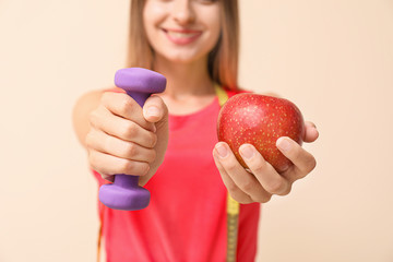 Sporty woman with dumbbell and apple on light background, closeup. Diet concept