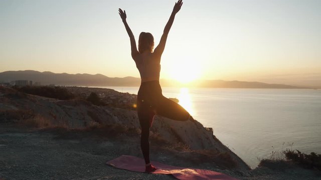 Silhouette of woman practices yoga and doing stretching at sunrise, slow motion