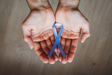 Man's hand holding a blue ribbon simbol of prostate cancer awareness month. Men's cancer concept.