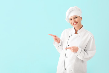 Beautiful female chef pointing at something on light background