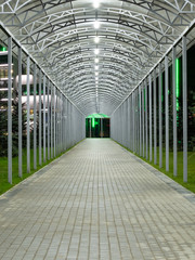 Futuristic pedestrian overpass tunnel with bright lighting, receding into the distance at night. Urban geometry.