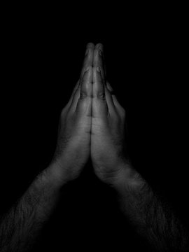 Low key black and white photo of a man with hands placed together showing the sign of namaste, the indian way of respectful greeting