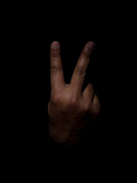Low key photo of a brown man showing the back of the hand with two fingers sticking out indicating the number two