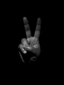 Low key black and white photo of a man showing two fingers indicating the number two or the victory sign