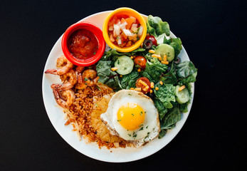 Asian Pineapple Fried rice with fried egg, shrimp,and vegetables on a white plate and black background