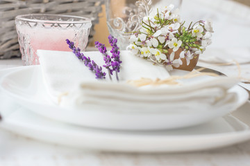 Fototapeta na wymiar Elegant table setting for wedding engagement Easter dinner with white ceramic plates cotton napkin tied with twine lavender flowers candles. Provence style