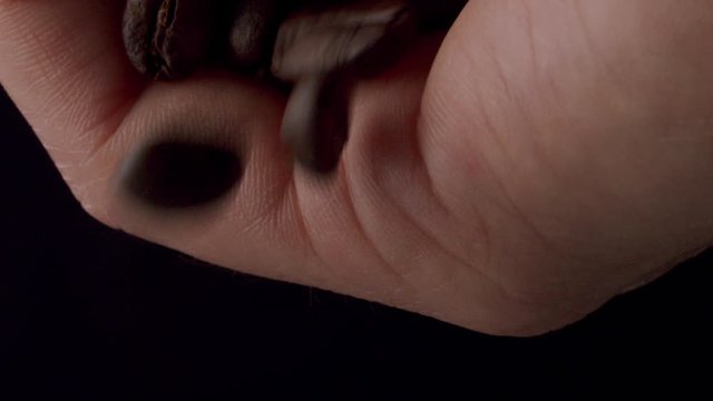 detail shot of coffee beans falling out of a caucasian hand in front of a black background.