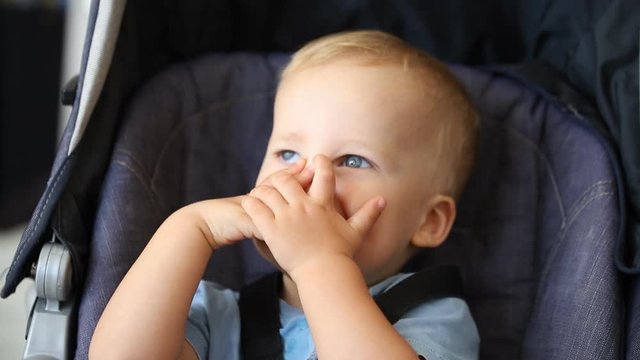 Cute adorable happy caucasian blond toddler boy sitting in stroller and laughing playing seek and hide game. Funny cheerful child smiling making peek-a-boo and closing face and eyes with hands