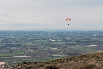 Paraglider flying over valley in Italy, cloudy sky