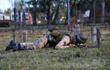 On a military training ground, exercises: Ukrainian soldier crawling under barbed wires