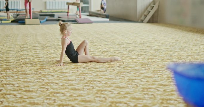 Little girl falling after handstand, performing handstand with split and falling on carpet while exercising during training in professional gym