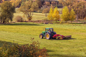 tractor on meadow cuts grass, hilly landscape, sunny day