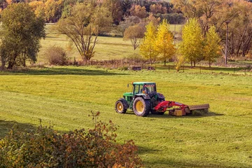 Schilderijen op glas tractor on meadow cuts grass, hilly landscape, sunny day © Roman