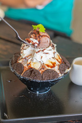 Eatting chocolate ice cream, whipping cream, banana slice topping on bingsu in black bowl on wooden table in cafe and restaurant. Delicious Korean shaved ice.
